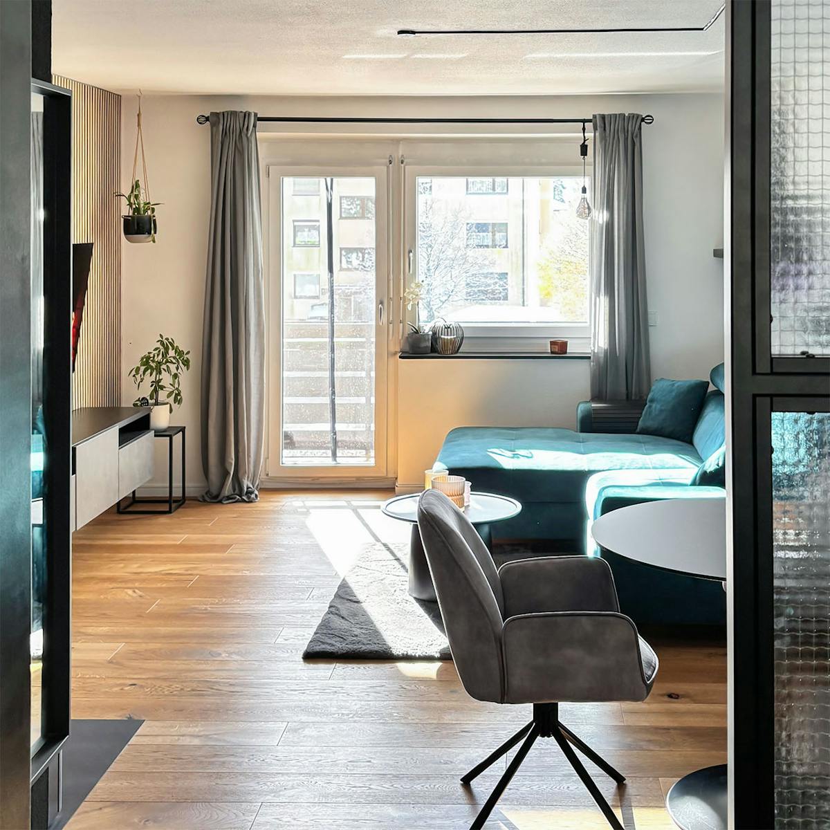 minimalistyczne mieszkanie z przestronnym salonem, w którym znajdują się turkusowa sofa, czarny stół i szare fotele