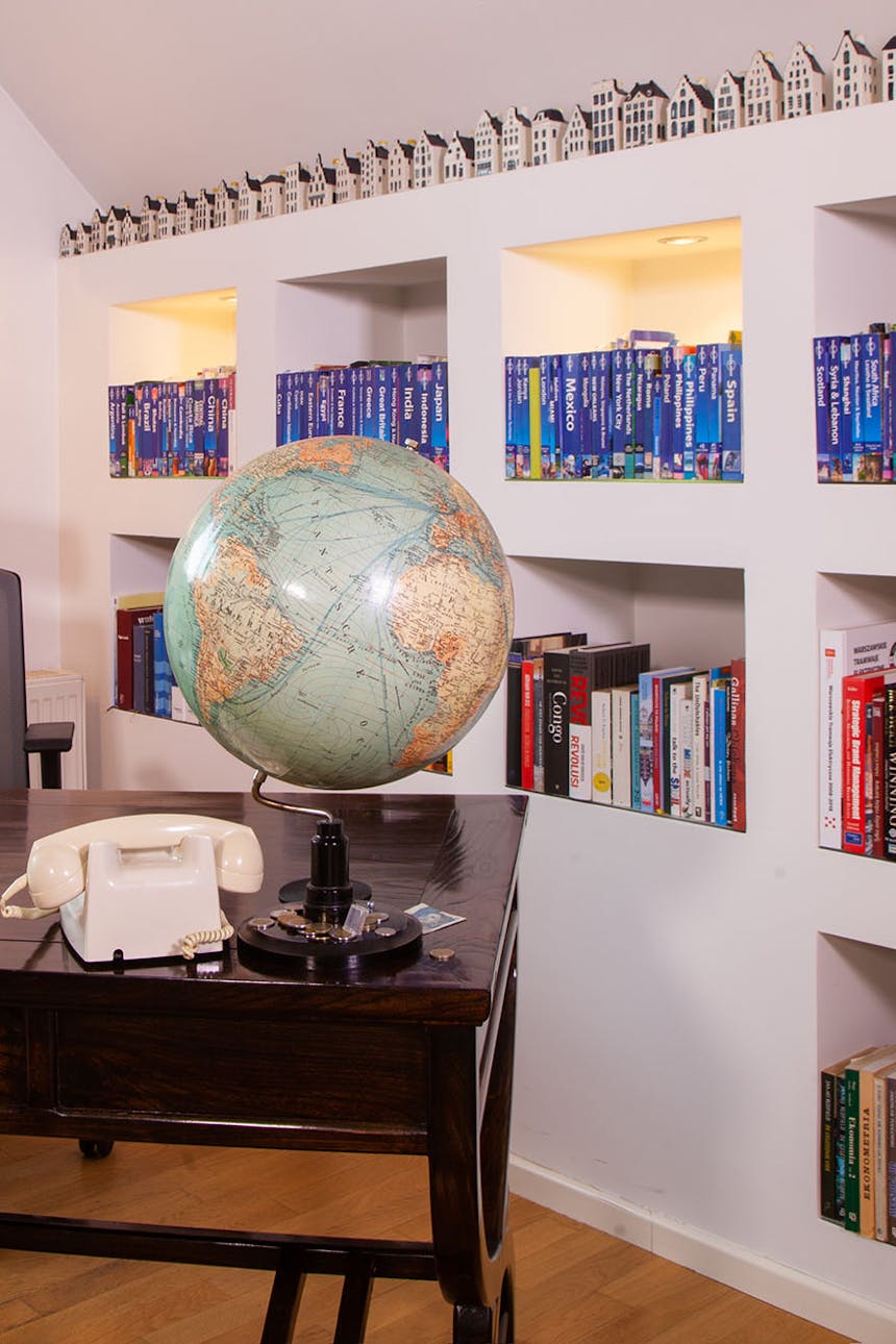 ein Globus und ein Telefon auf einem dunkelbraunen Schreibtisch neben einer Wand mit Regalen voller Bücher