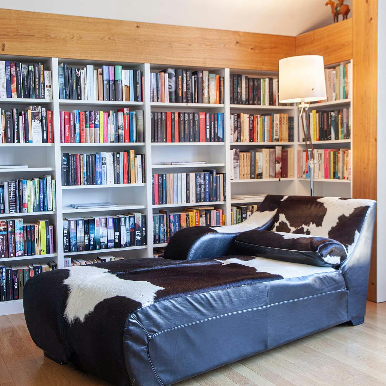 a chaise lounge with black and white upholstery next to a wall filled with bookshelves