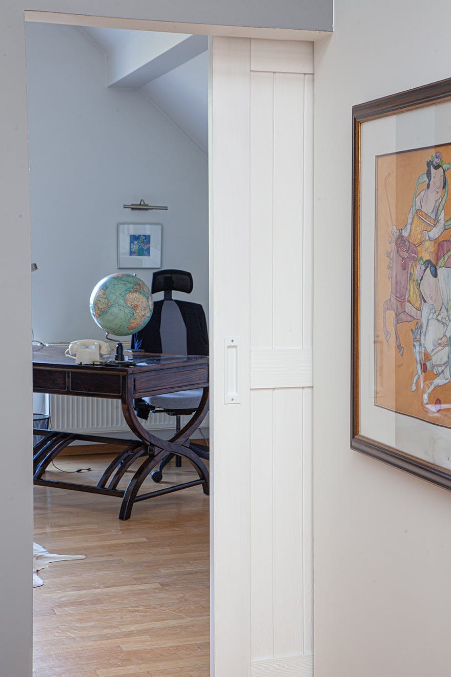 an open white door revealing part of a home office with a dark desk