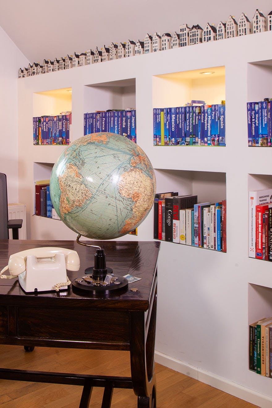 a globe and a telephone on a dark brown desk next to a wall with shelves filled with books