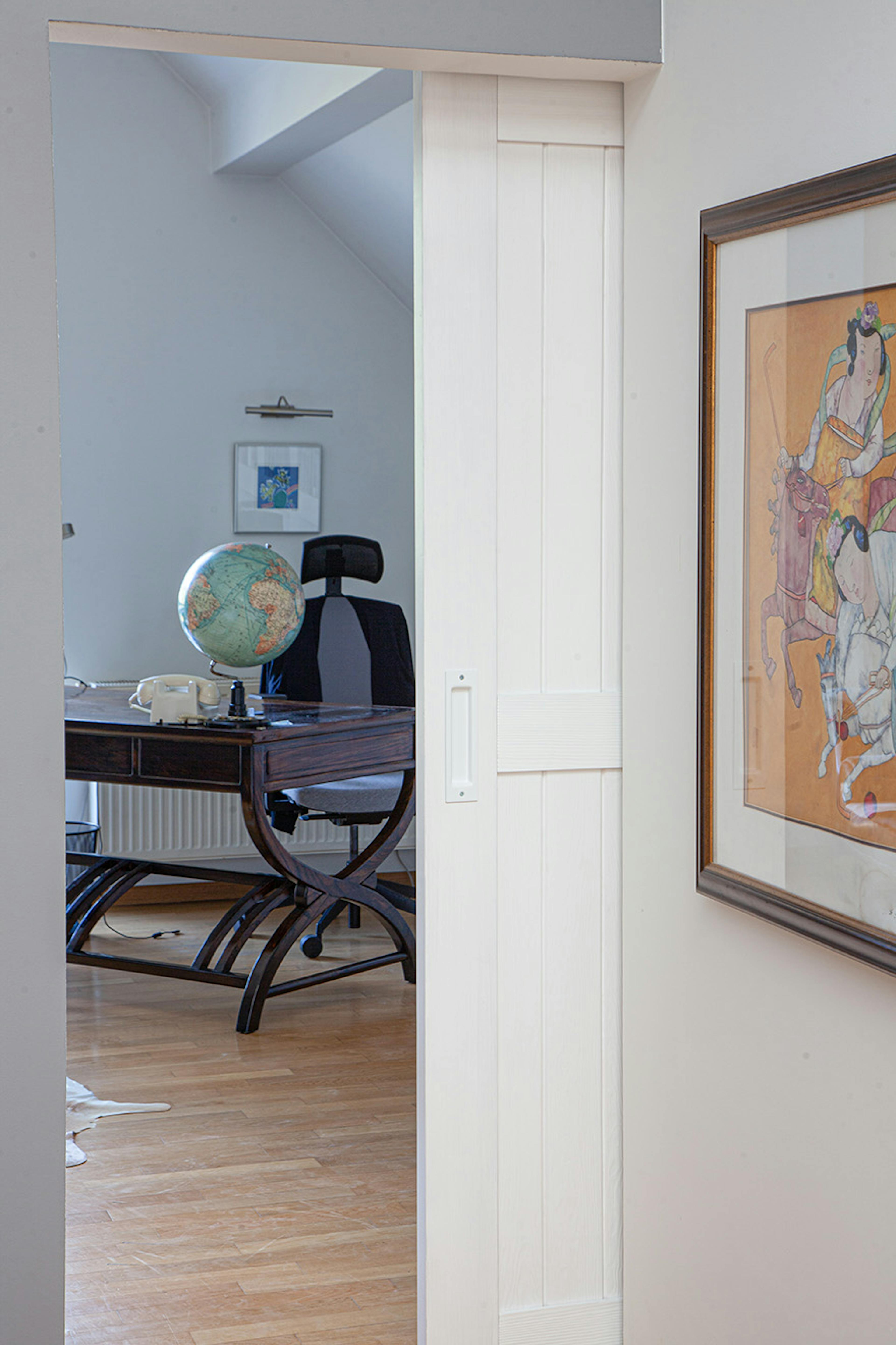 une porte blanche ouverte révélant une partie d'un bureau à domicile avec un bureau sombre