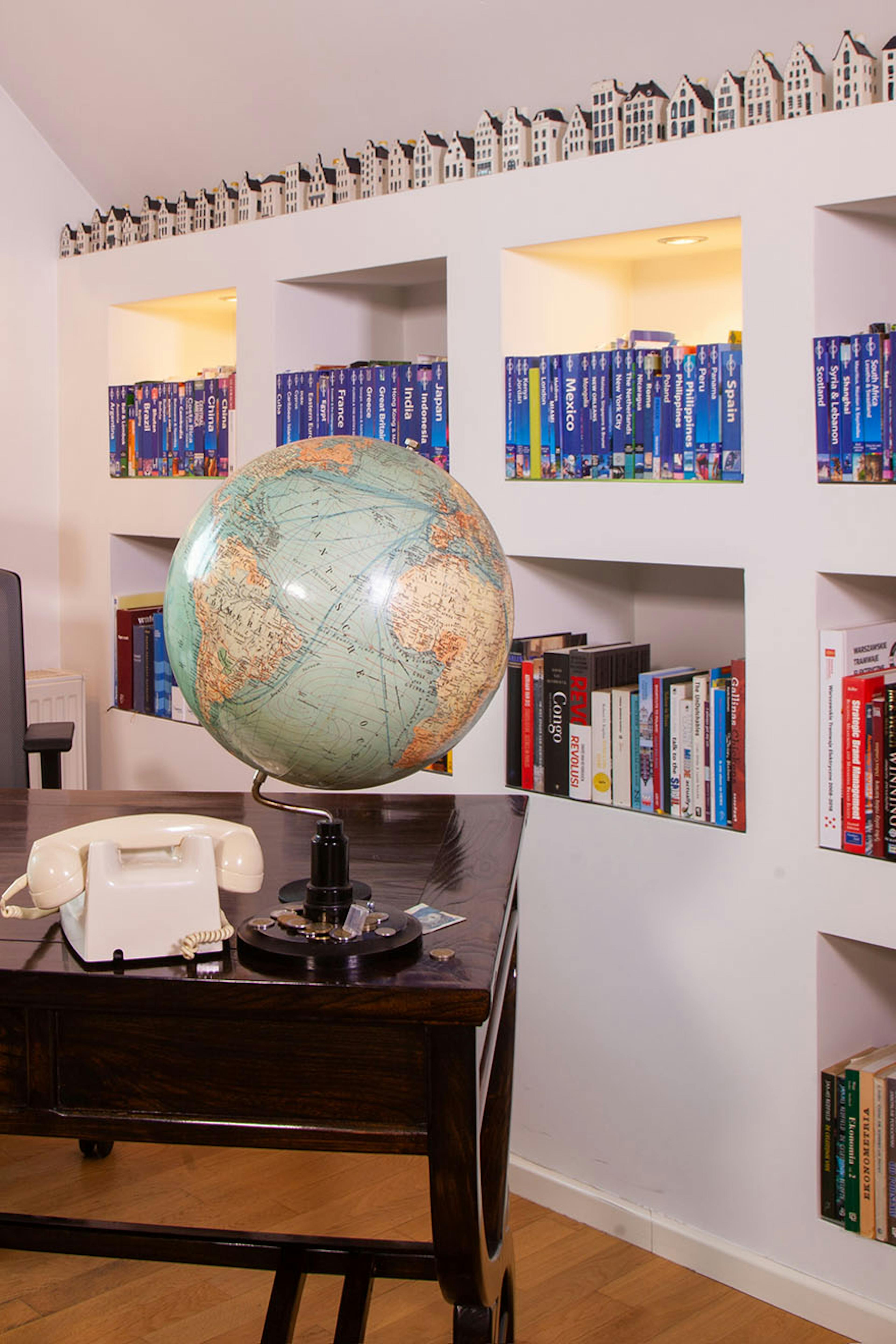 un globe et un téléphone sur un bureau marron foncé contre un mur avec des étagères remplies de livres