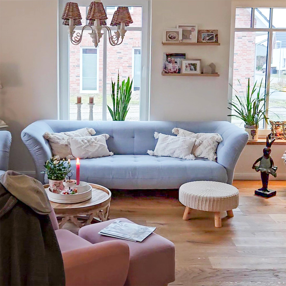 salon z jasnoniebieską sofą i białymi poduszkami, drewnianym stolikiem kawowym oraz pufą z pleconym siedziskiem