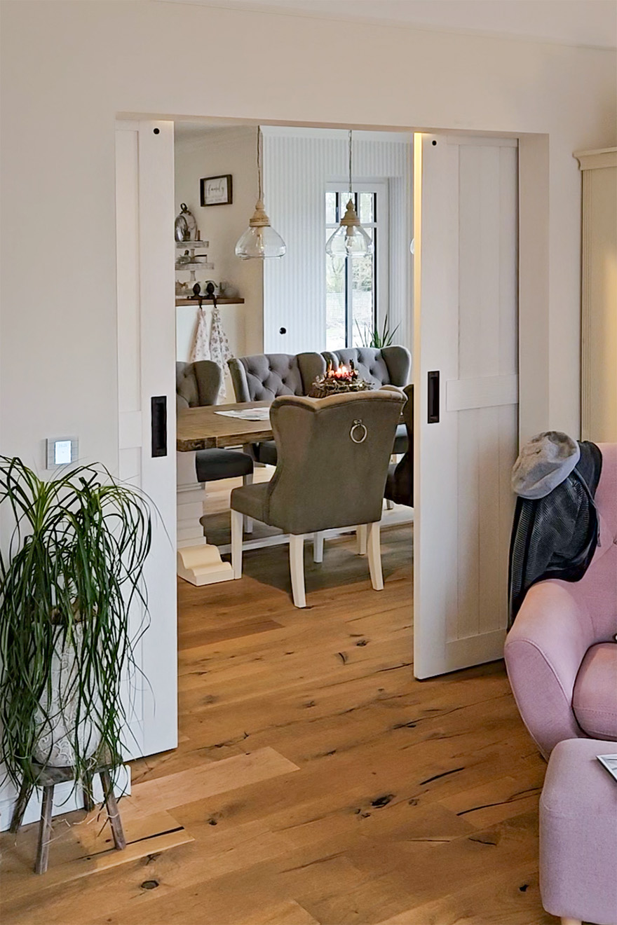 Offene Schiebetüren geben den Blick auf einen Teil des Esszimmers mit einem großen Tisch und grauen Stühlen frei