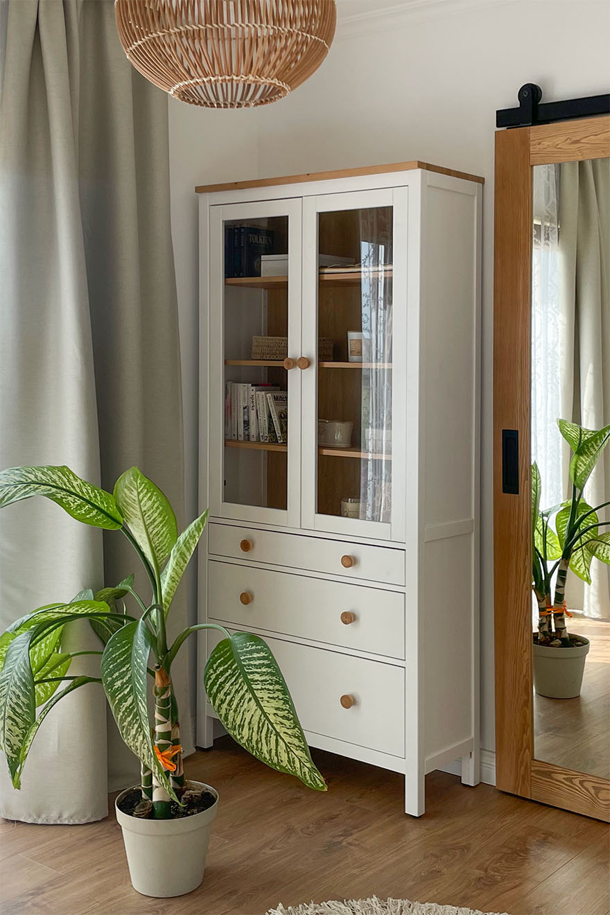 eine weiße Vitrine mit Schubladen und Glastüren und eine große Topfpflanze im Schlafzimmer