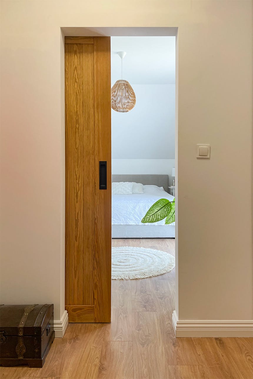 uchylone drzwi przesuwne ukazujące fragment dużego łóżka w sypialni