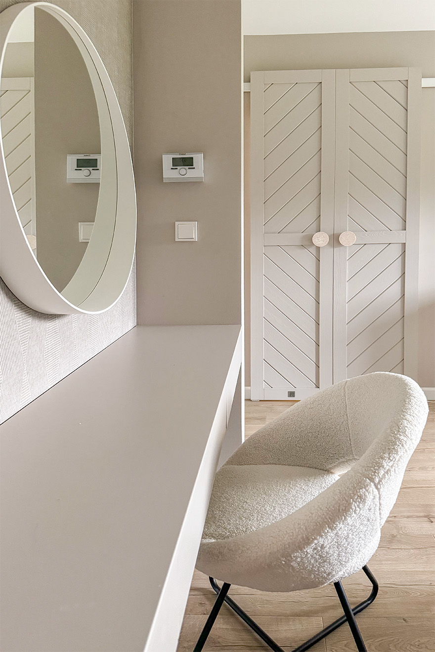 kremowe krzesło tapicerowane przy toaletce z okrągłym lustrem w białej ramie