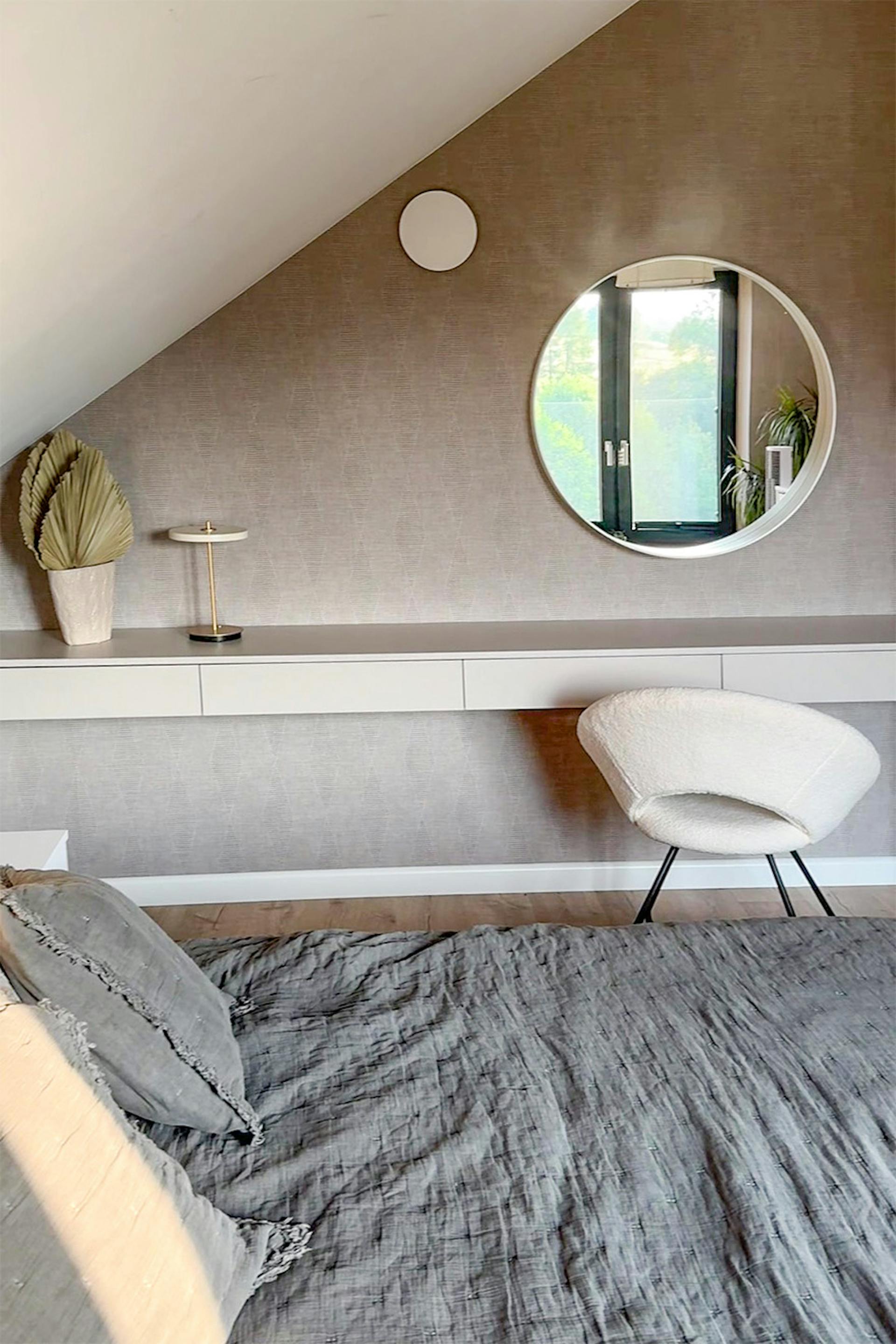 ein Bett mit grauer Tagesdecke und einem Schminktisch in einem minimalistischen Schlafzimmer mit Dachschräge