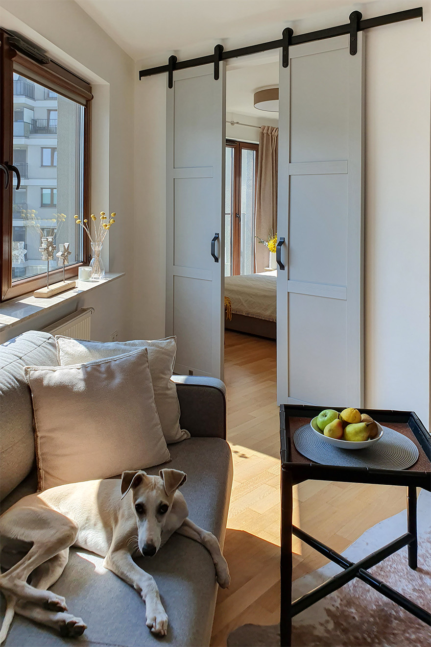 sofa i stolik kawowy przed drzwiami przesuwnymi prowadzącymi z salonu do sypialni