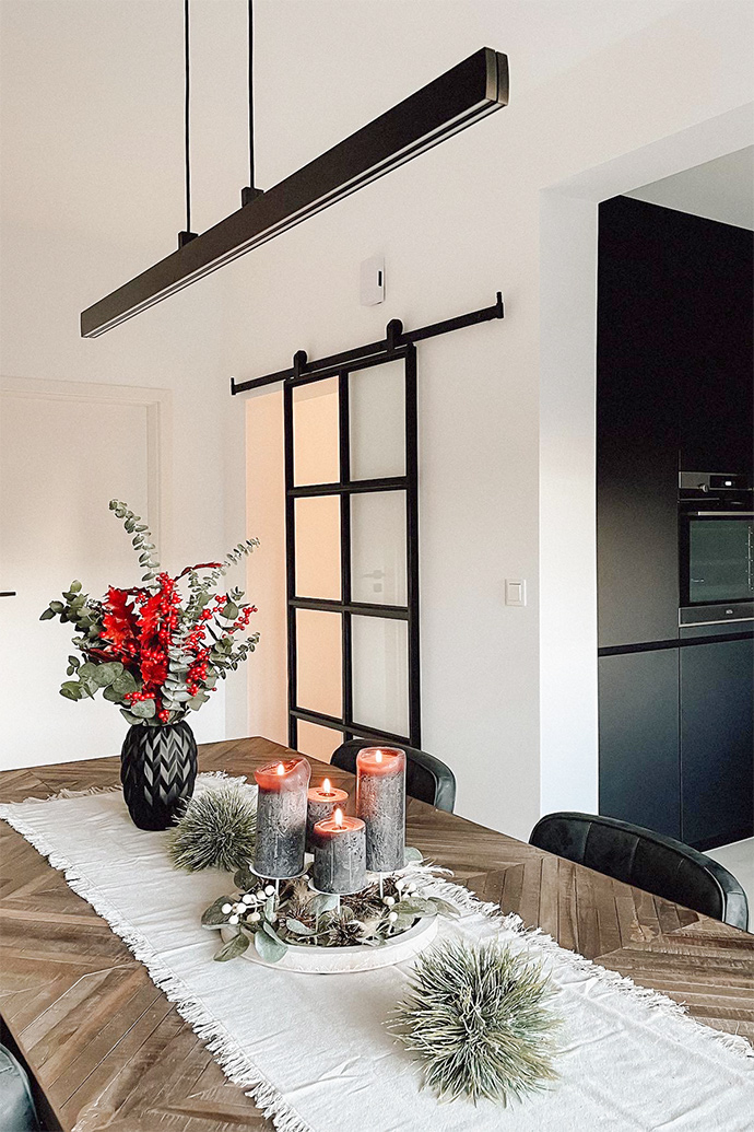 dekoracyjne świece, wazon z suszonymi kwiatami na drewnianym stole jadalnianym oświetlonym długą, minimalistyczną lampą