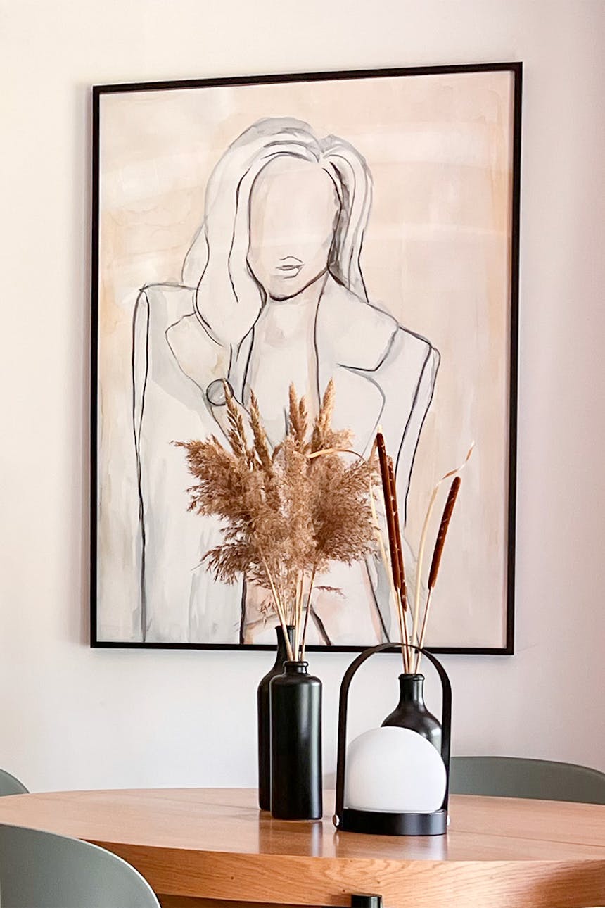 duży plakat w beżowo-brązowej tonacji w cienkiej czarnej ramie wiszący na ścianie nad okrągłym stołem