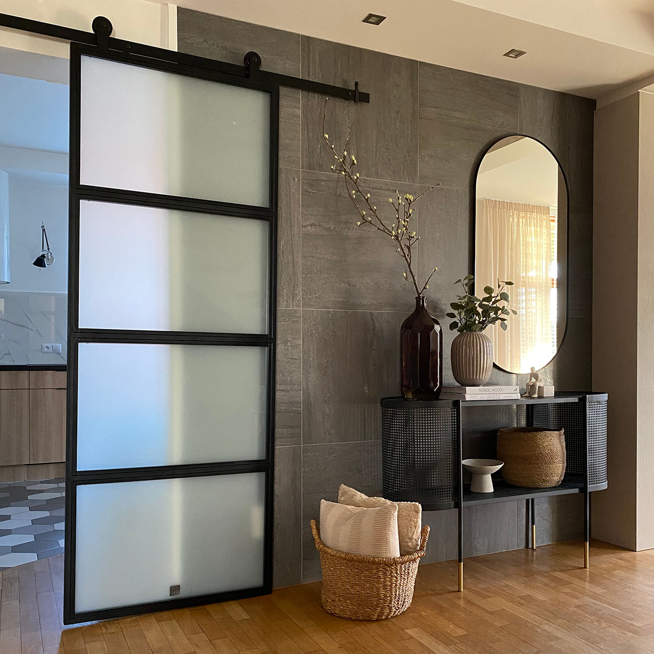 Loft Türen mit glas, Metalltür mit Glas für die Küche, helle Küche mit Kochinsel, Graphitfliesen an der Wand, schwarze durchbrochene Konsole mit Spiegel im Flur, Weidenkorb mit Kissen