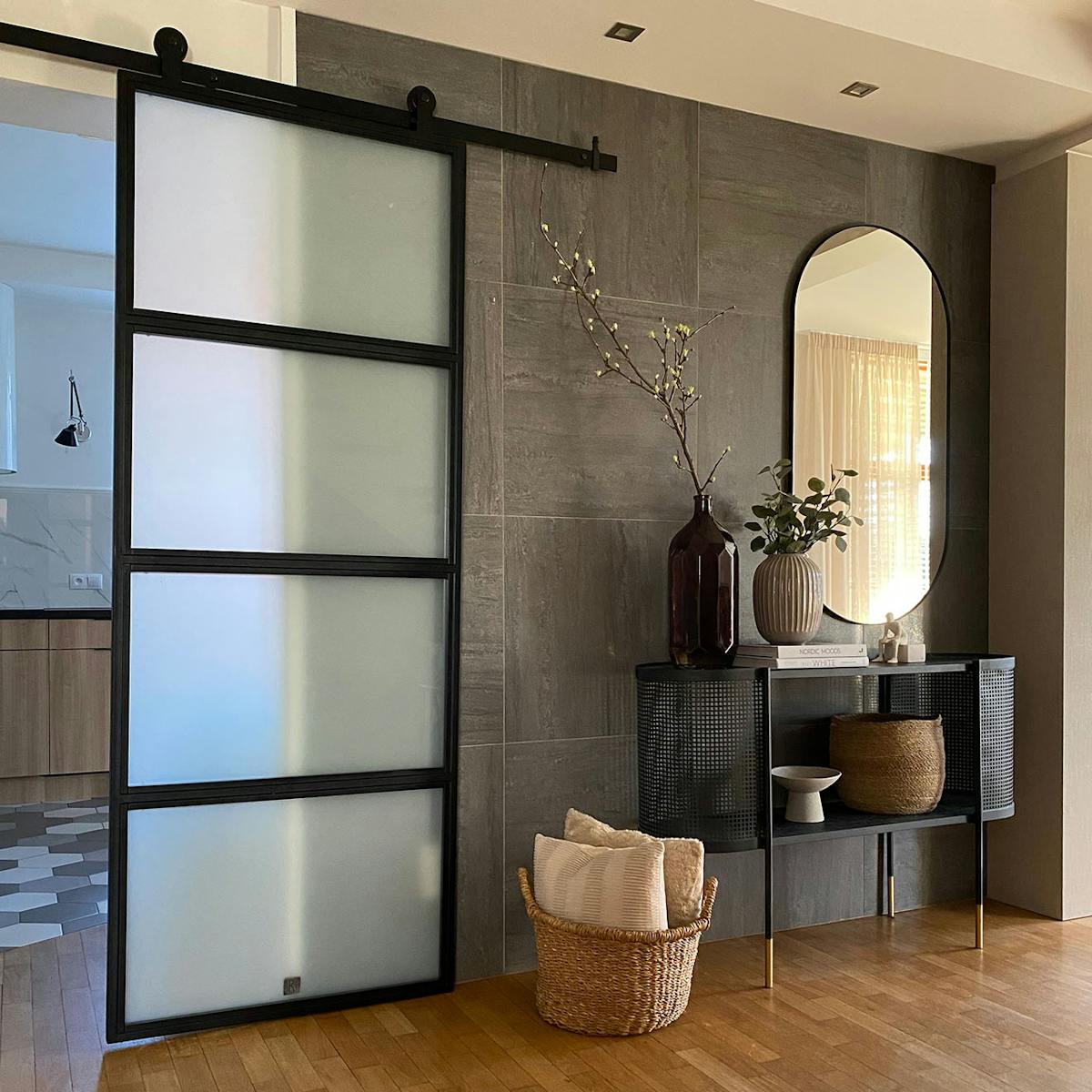 Loft Türen mit glas, Metalltür mit Glas für die Küche, helle Küche mit Kochinsel, Graphitfliesen an der Wand, schwarze durchbrochene Konsole mit Spiegel im Flur, Weidenkorb mit Kissen