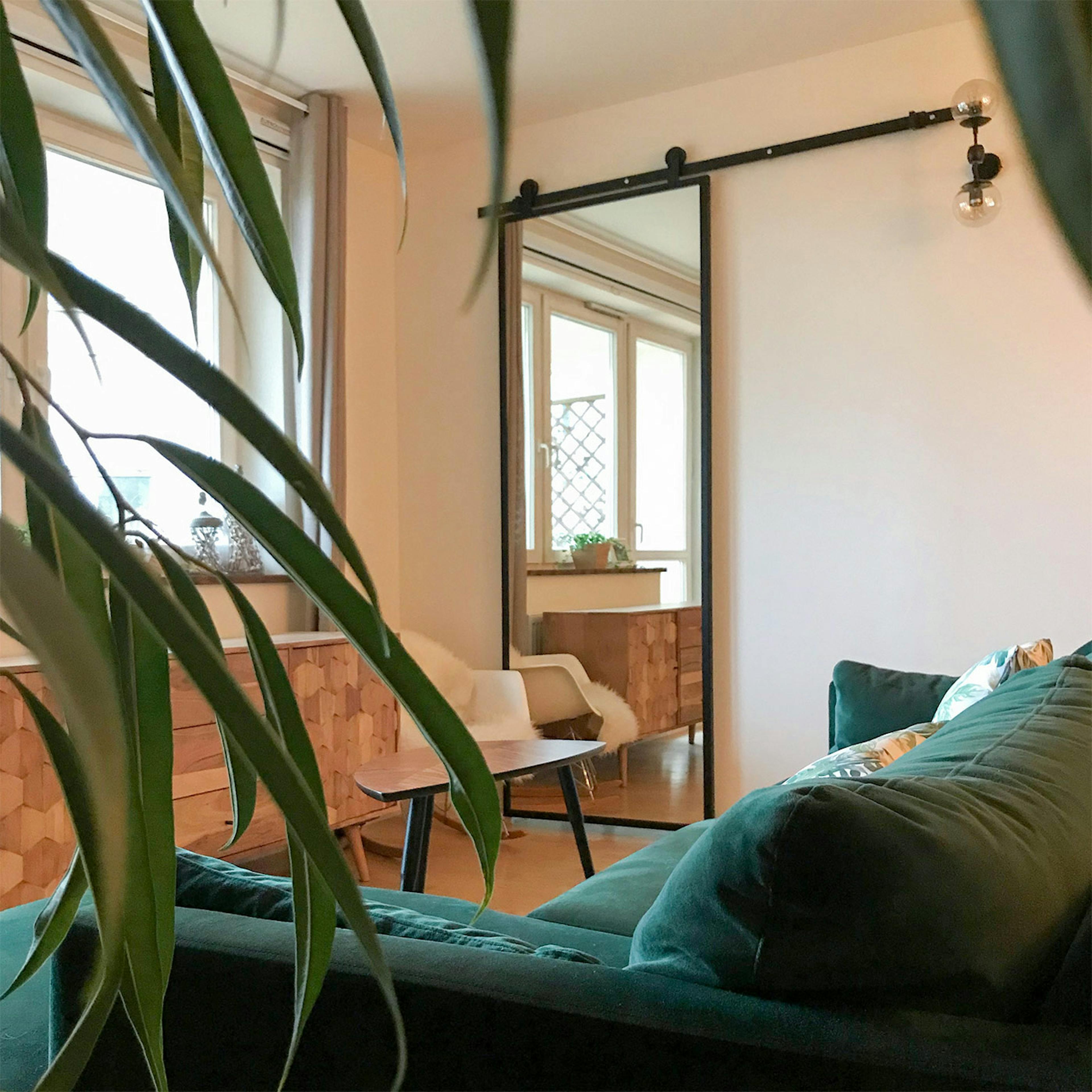 sliding door with a mirror, door with a mirror in a metal frame, sliding door in a modern interior, green sofa, large mirror in the living room