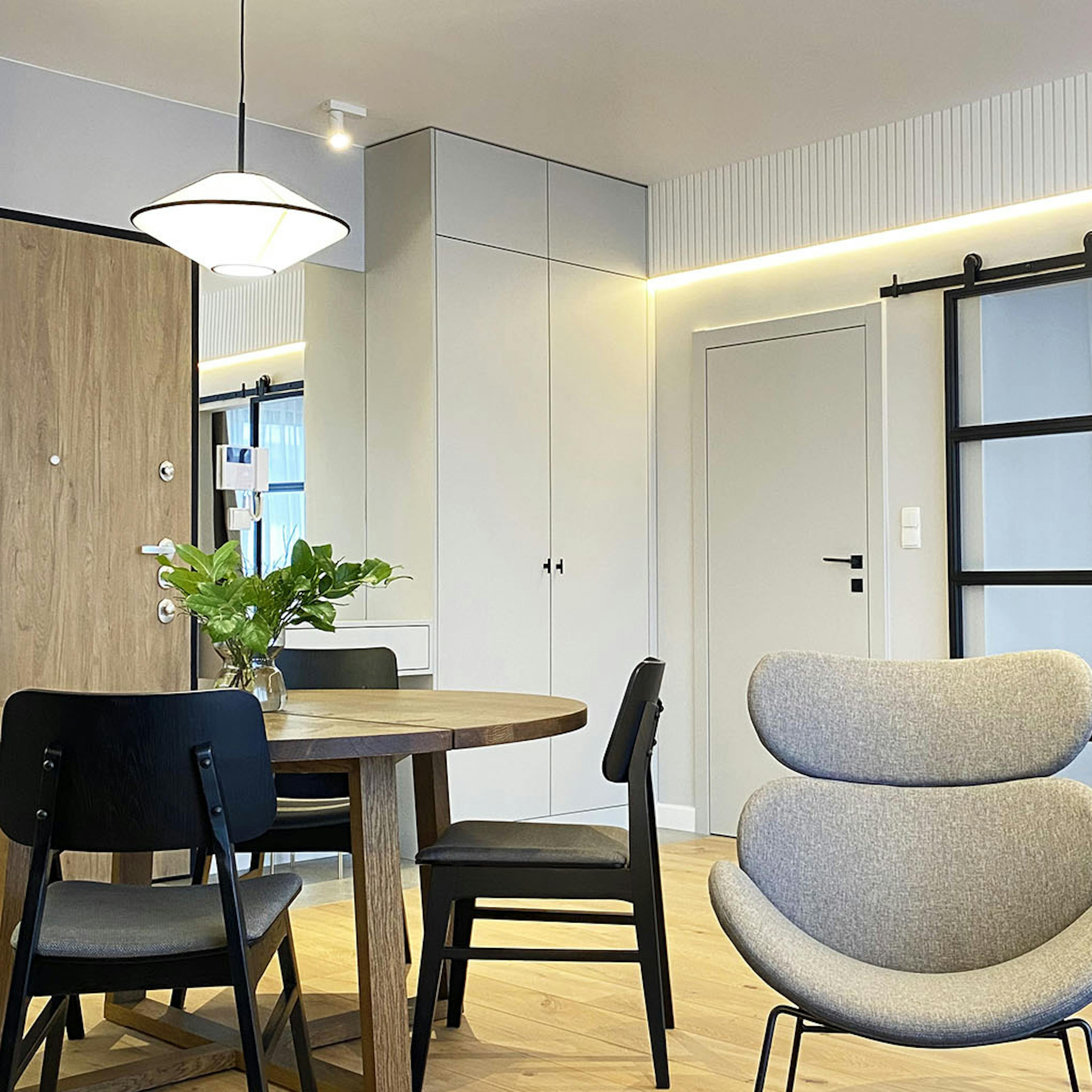 une table ronde blanche, des fauteuils gris sur une structure en métal, des murs blancs et un sol clair dans un appartement moderne