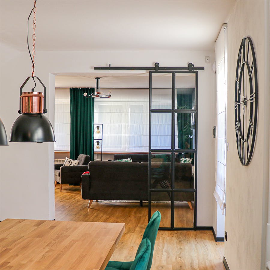 black metal wall clock, industrial style clock, loft decor, metal door with glass, loft door, metal glass sliding door, black glass door, green dining chairs, living room open to dining room, industrial hanging lamps for dining room, large wooden dining table