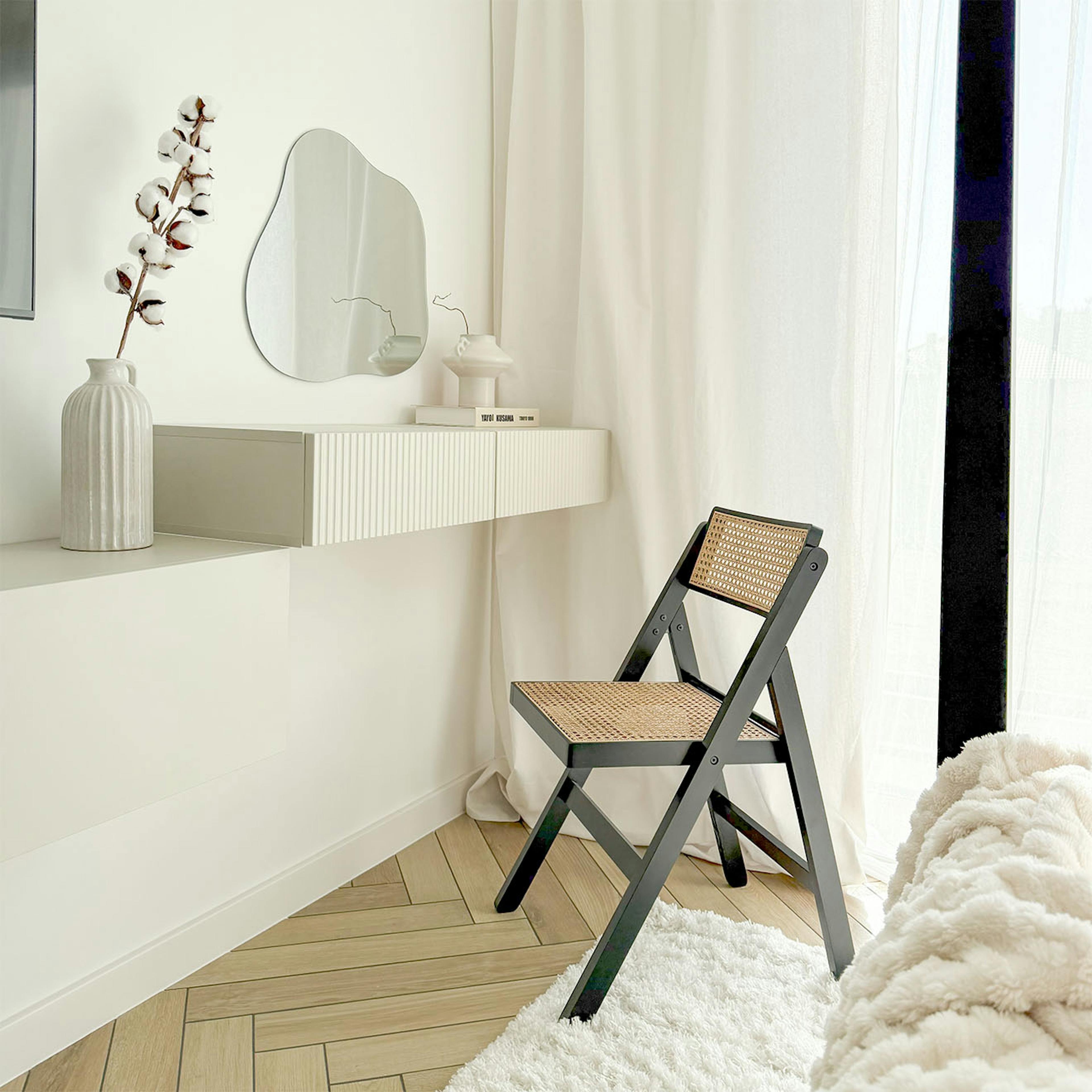 coiffeuse minimaliste avec un miroir mural de forme unique et une élégante chaise pliante noire avec un siège en rotin