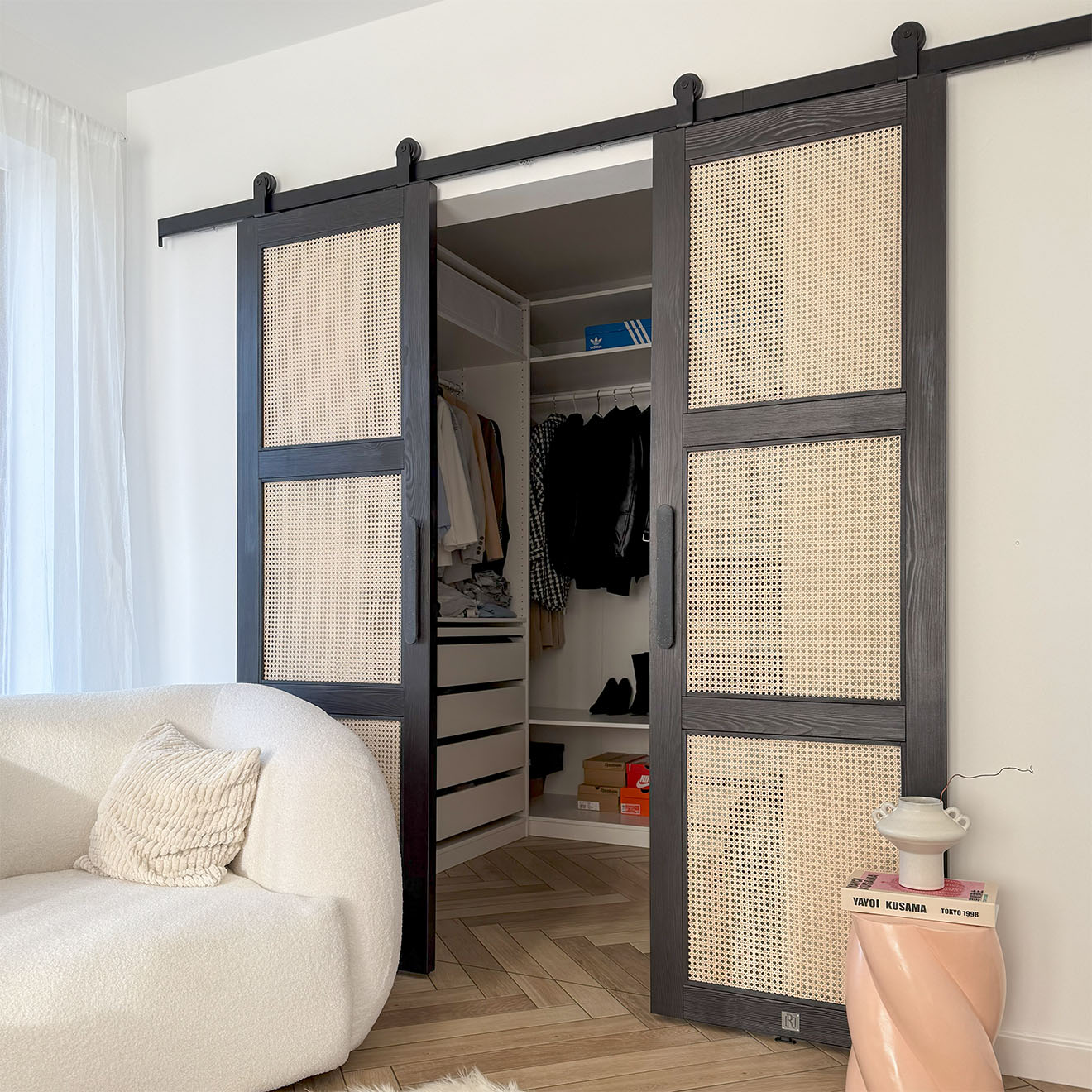 Modernes Schlafzimmer-Interieur mit offenen schwarzen Rattan-Schiebetüren, die einen minimalistischen Ankleidezmimmer und einen weißen strukturierten Sessel freigeben