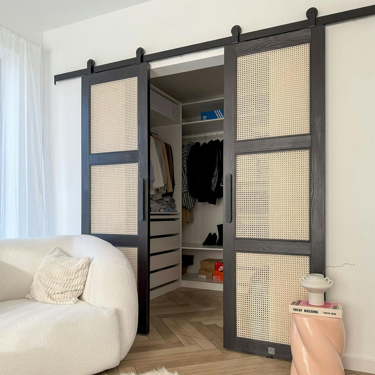 Modernes Schlafzimmer-Interieur mit offenen schwarzen Rattan-Schiebetüren, die einen minimalistischen Ankleidezmimmer und einen weißen strukturierten Sessel freigeben