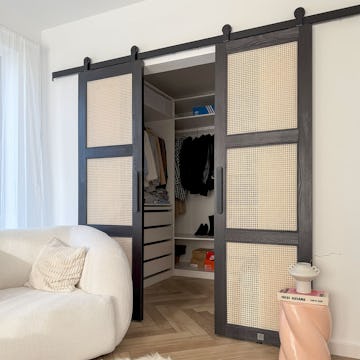 Modernes Schlafzimmer-Interieur mit offenen schwarzen Rattan-Schiebetüren, die einen minimalistischen Ankleidezmimmer und einen weißen strukturierten Sessel freigeben