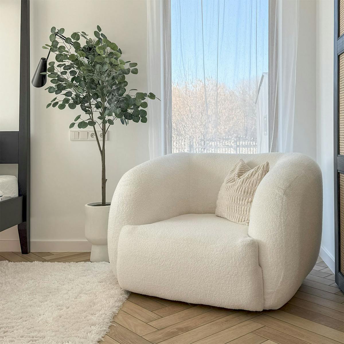 ein gemütlicher weißer Sessel mit strukturiertem Kissen steht neben einem weichen weißen Teppich und einer Topfpflanze