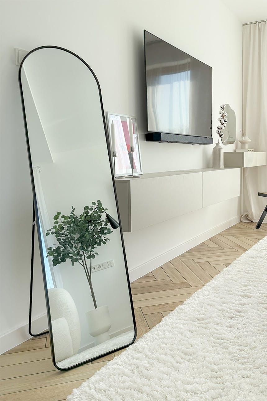 eine Ecke in einem modernen Schlafzimmer mit einem großen schwarzen gewölbten Spiegel an einer weißen Wand, einem an der Wand montierten Fernseher und einer hängenden Konsole