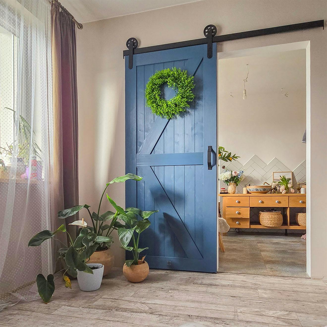 blue sliding barn door connecting bedroom to bathroom; green wreath on door; potted plants by door