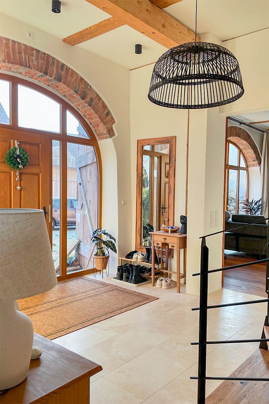 Moderner Eingangsbereich im Landhausstil mit beigefarbenen Fliesen, großen gewölbten Türen und Fenstern, einer Hängelampe und Holzakzenten.