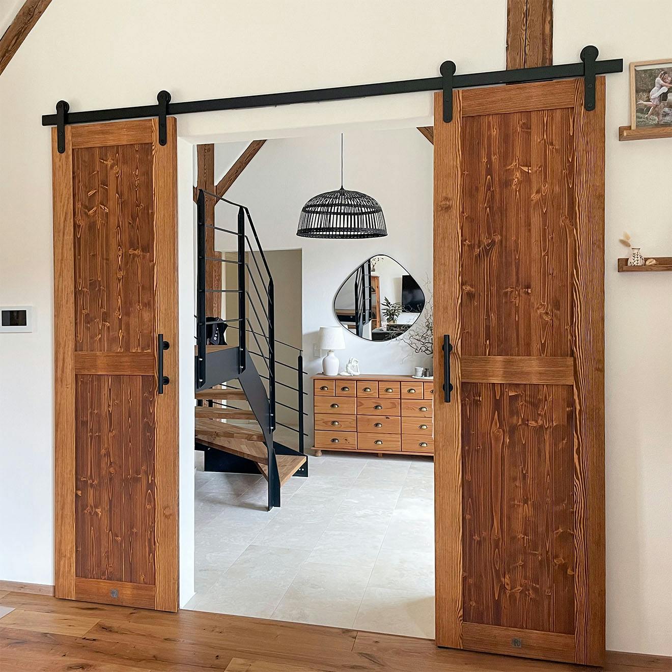 Double wooden, rustic sliding barn doors with black fittings open to a spacious foyer with wooden stairs, mirror and chest of drawers.
