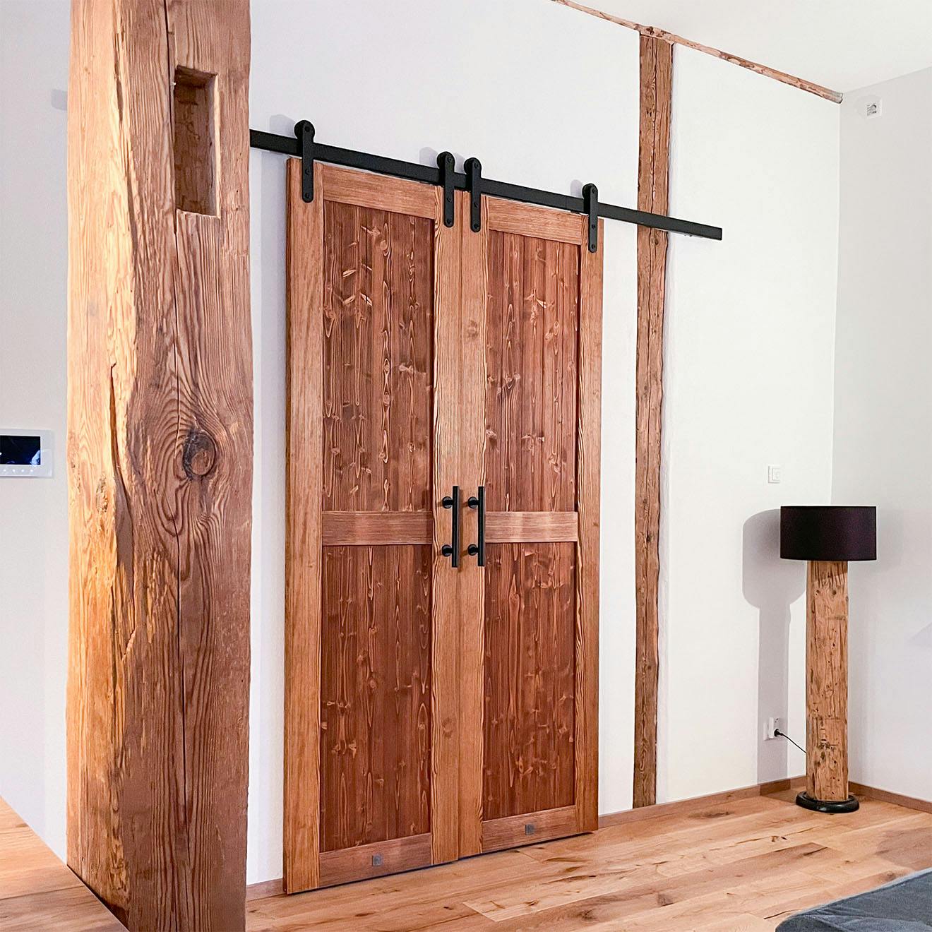 Closed double wooden sliding barn doors with black fittings and handles mounted on a white wall.