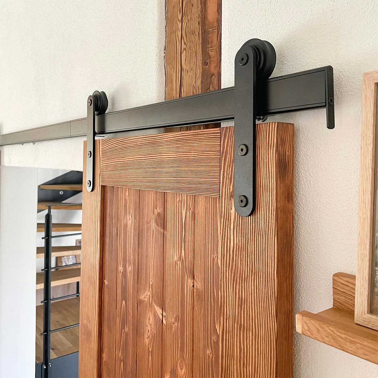 Close-up of the black metal fittings and rollers of a sliding barn door mounted on a brown wooden door.
