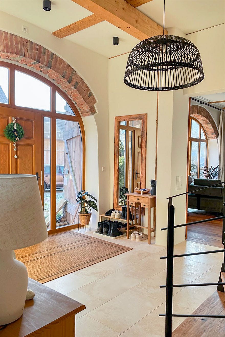 Modern country style entryway with beige tiles, large arched doorway and windows, pendant lamp and wood accents.