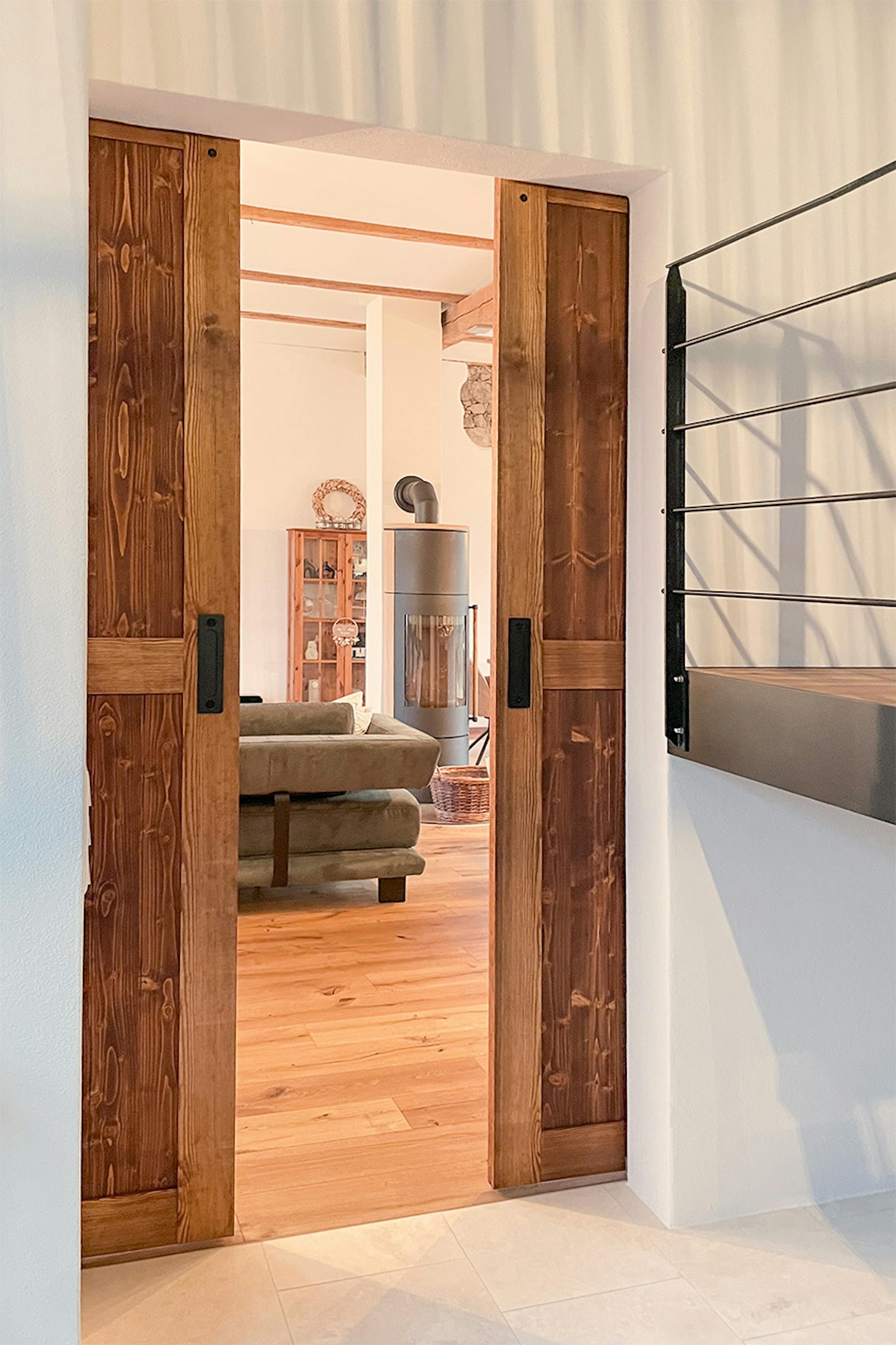 Portes de grange coulissantes en bois ouvertes menant à un salon lumineux avec parquet, poêle indépendant et canapé foncé.