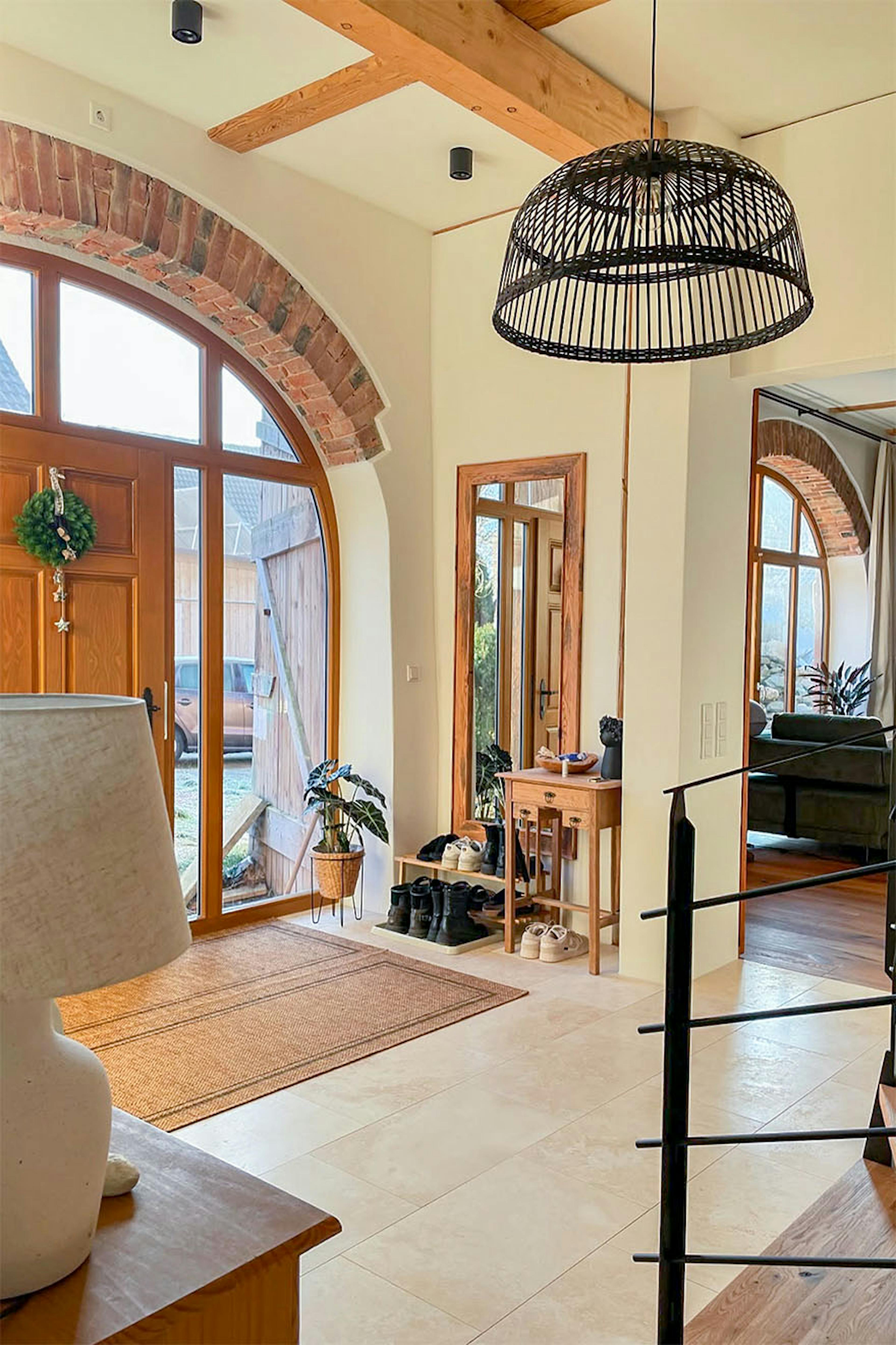 Entrée de style campagnard moderne avec carrelage beige, grande porte et fenêtres cintrées, lampe suspendue et accents de bois.