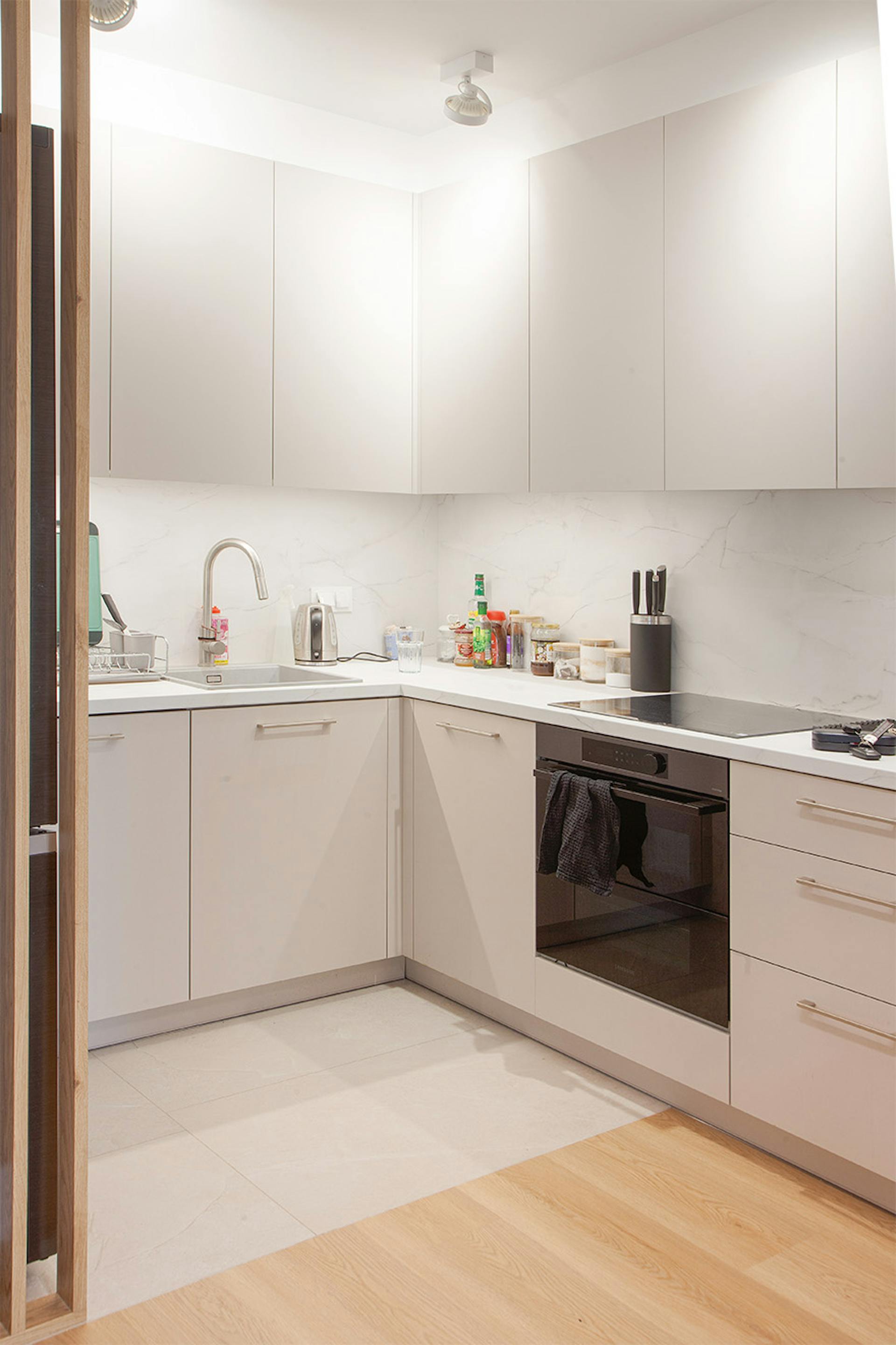 Nowoczesna, jasna kuchnia z jasnoszarymi szafkami i białym blatem.