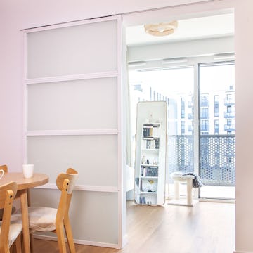 Offene, weiße Schiebetüren mit Milchglas, die einen Teil eines hellen Zimmers mit einem großen, stehenden Spiegel und einem Kratzbaum für die Katze zeigen.