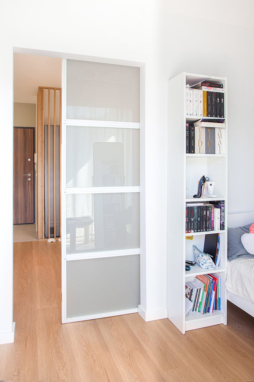 Weiße Schiebetüren mit Milchglas, die das Schlafzimmer mit einem Bücherregal vom Flur mit Holzlamellen trennen.