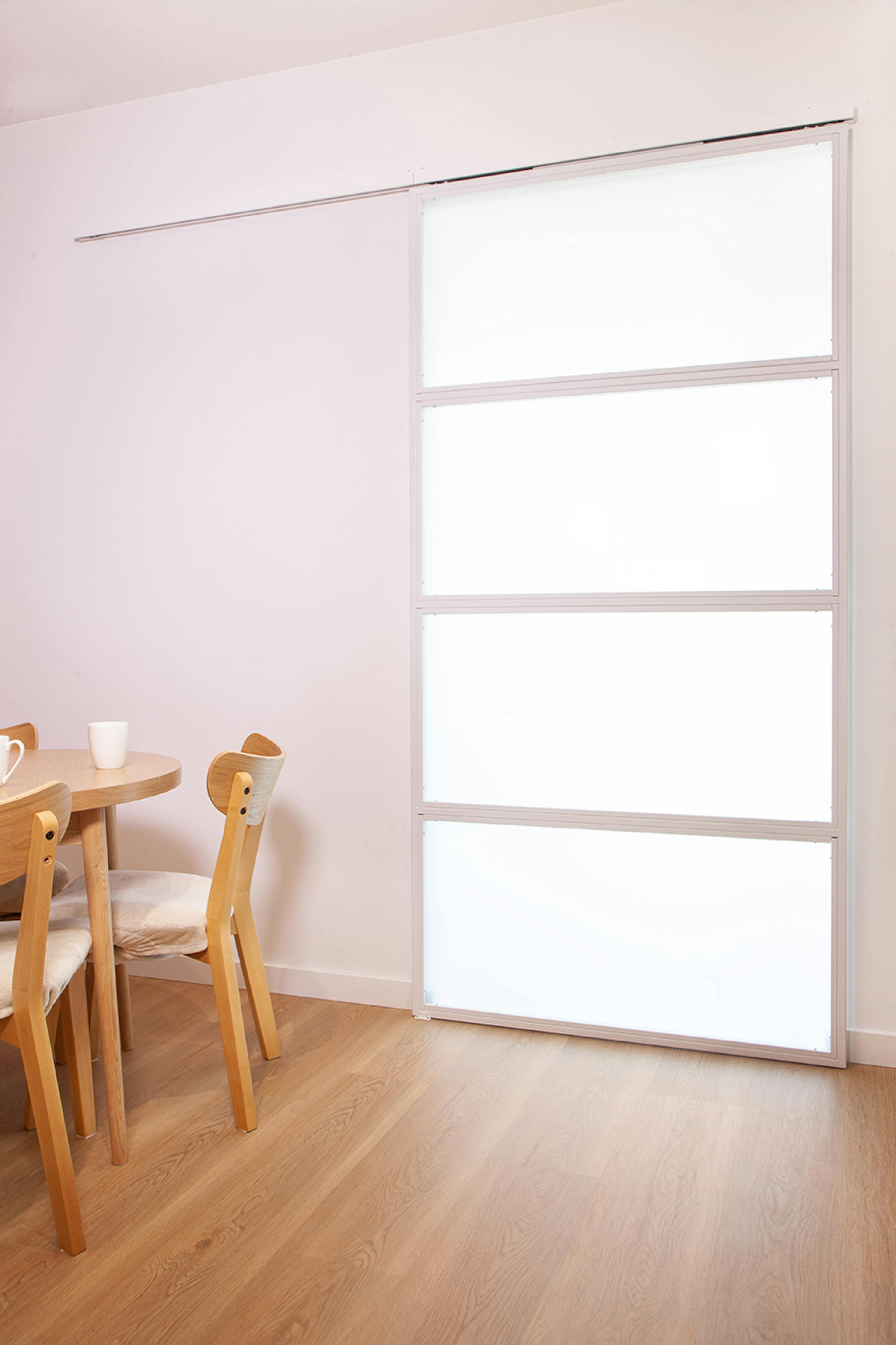 Porte coulissante blanche fermée avec quatre panneaux en verre dépoli, à côté d'une table ronde avec des chaises en bois.