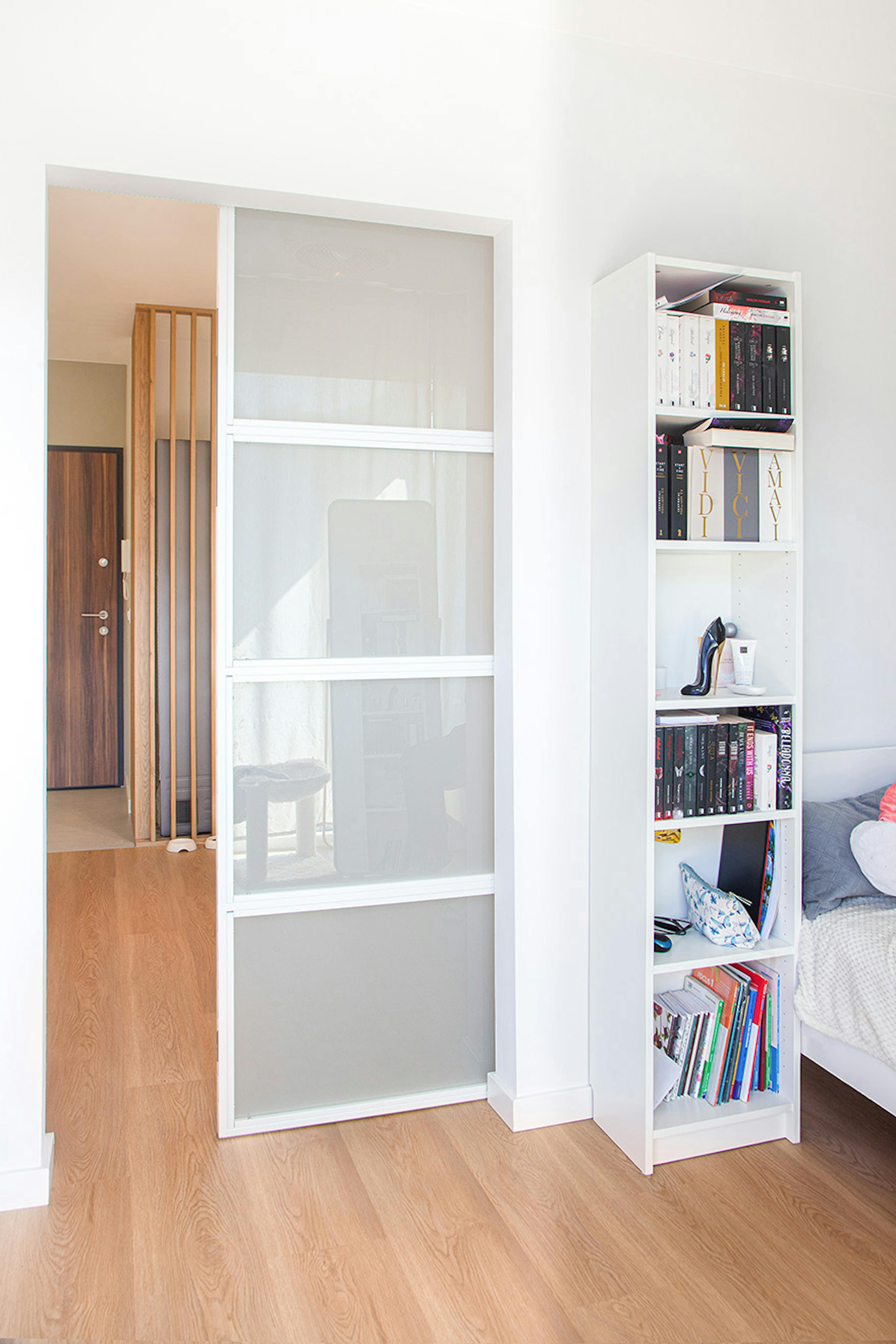 Porte coulissante blanche en verre dépoli, séparant la chambre avec une bibliothèque du couloir avec des lamelles en bois.