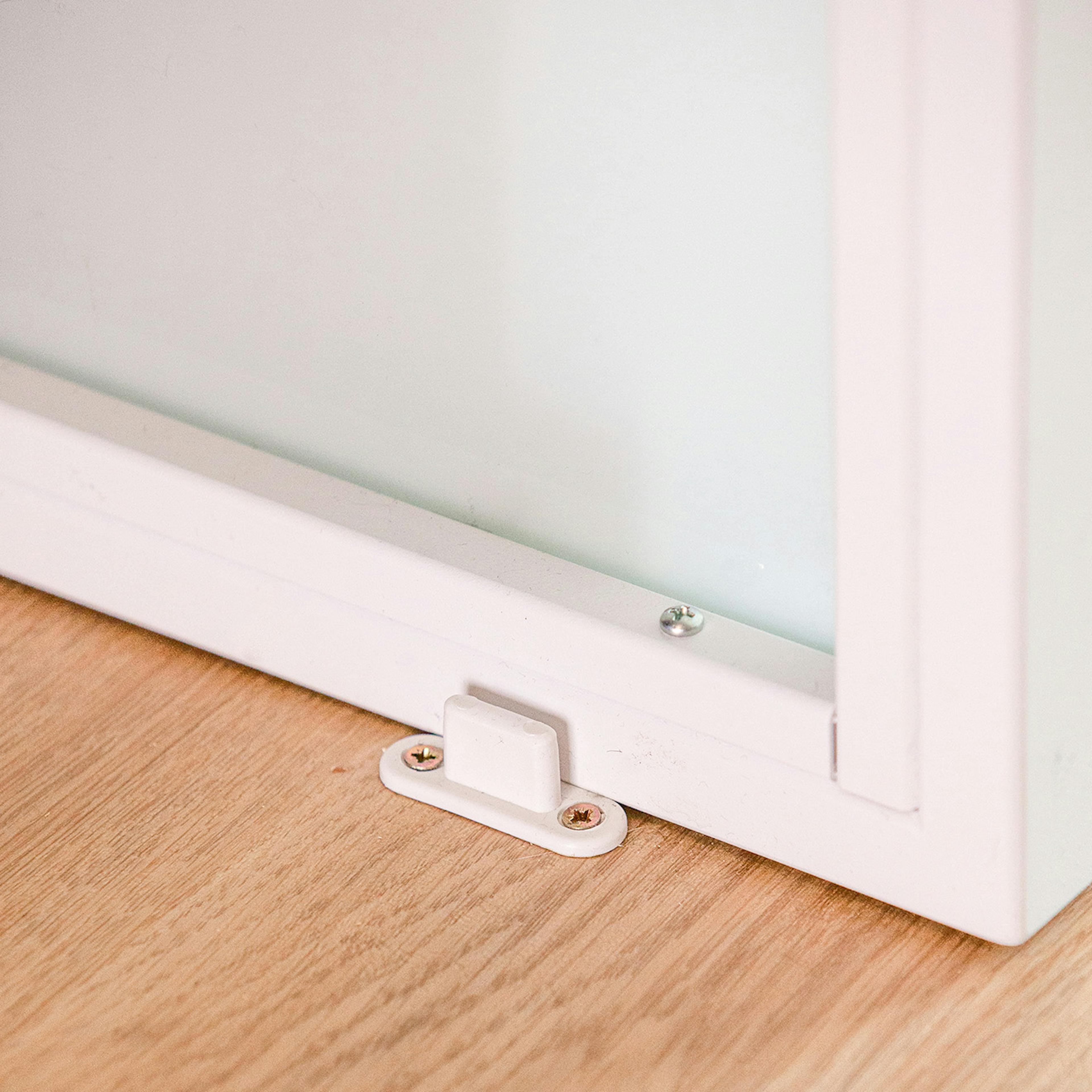 Détail d'une butée de sol blanche près du cadre inférieur d'une porte coulissante blanche, fixée au parquet en bois.