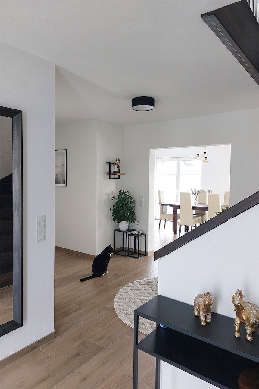 Przedpokój w nowoczesnym domu z jasną podłogą. Widok na jadalnię z drewnianym stołem i kremowymi krzesłami.