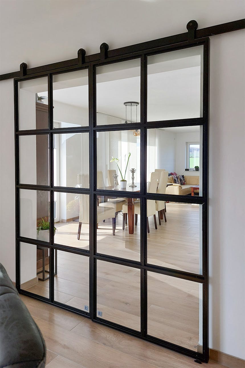 Widok ogólny podwójnych czarnych drzwi przesuwnych oddzielających strefy; widok na jasne wnętrze salonu i jadalni.
