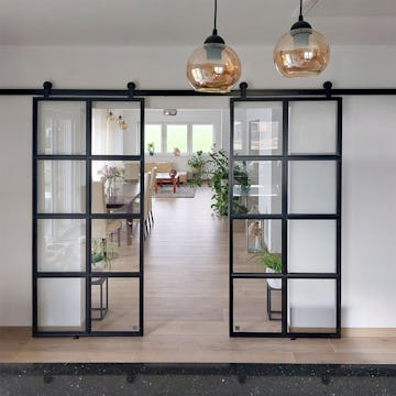 Schwarze Industrie-Schiebetüren trennen die Küche vom Wohnzimmer; ein modernes Interieur mit klassischen Elementen und natürlichem Licht.