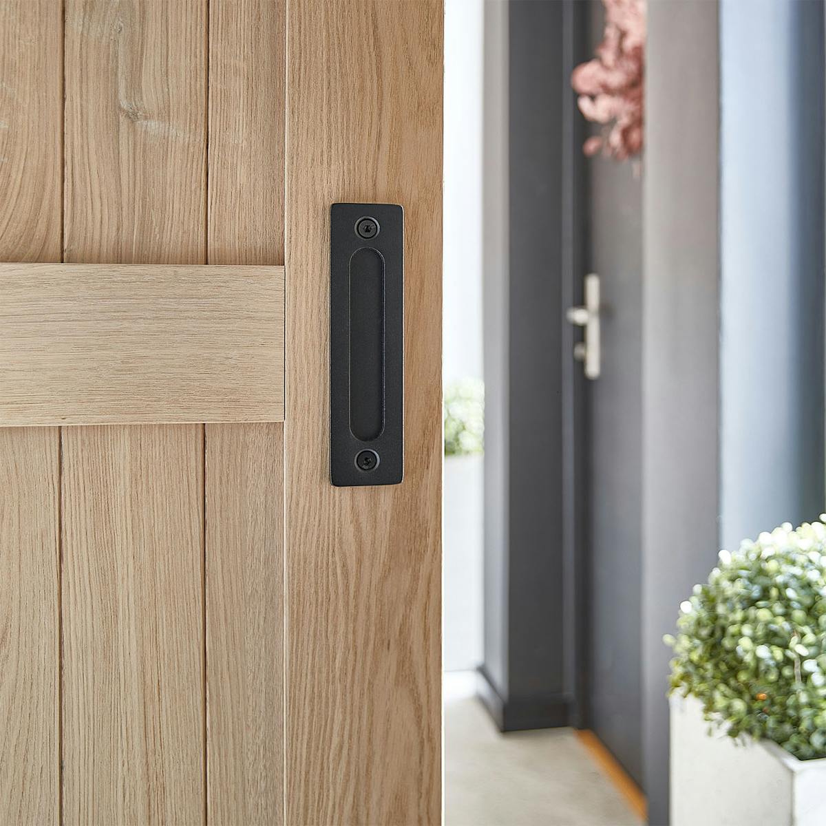 Wpuszczony, czarny uchwyt w dębowych drzwiach przesuwnych. Detal uchwytu świadczy o dbałości o szczegóły i minimalistycznym designie.