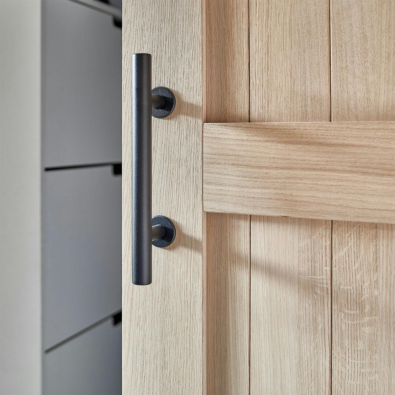 Detail of a black handle for an oak sliding door. The handle, shaped like a straight, matte tube, emphasizes the modern, minimalist style.