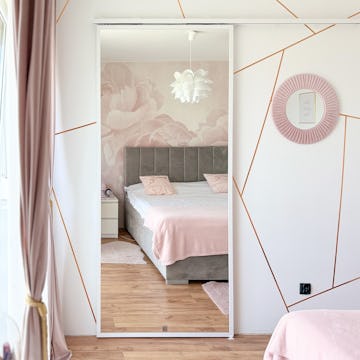 Nowoczesna sypialnia w pudrowym różu i szarości; Duże lustro na drzwiach przesuwnych; Fototapeta z różami za łóżkiem; Złote linie geometryczne na ścianie.