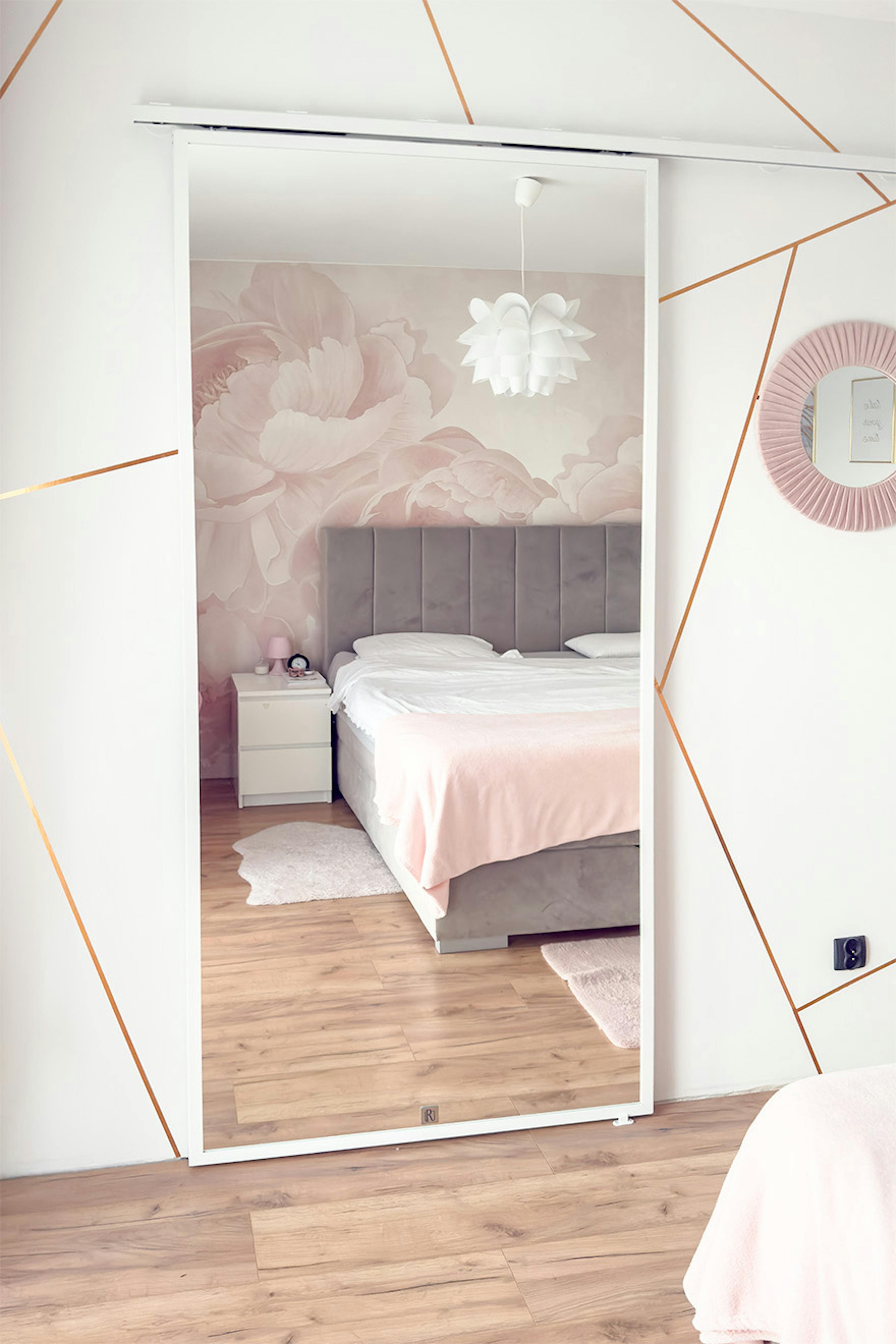 Porte coulissante avec miroir pour le dressing ; chambre à coucher avec lit et tête de lit matelassée grise ; miroir agrandissant visuellement l'intérieur.