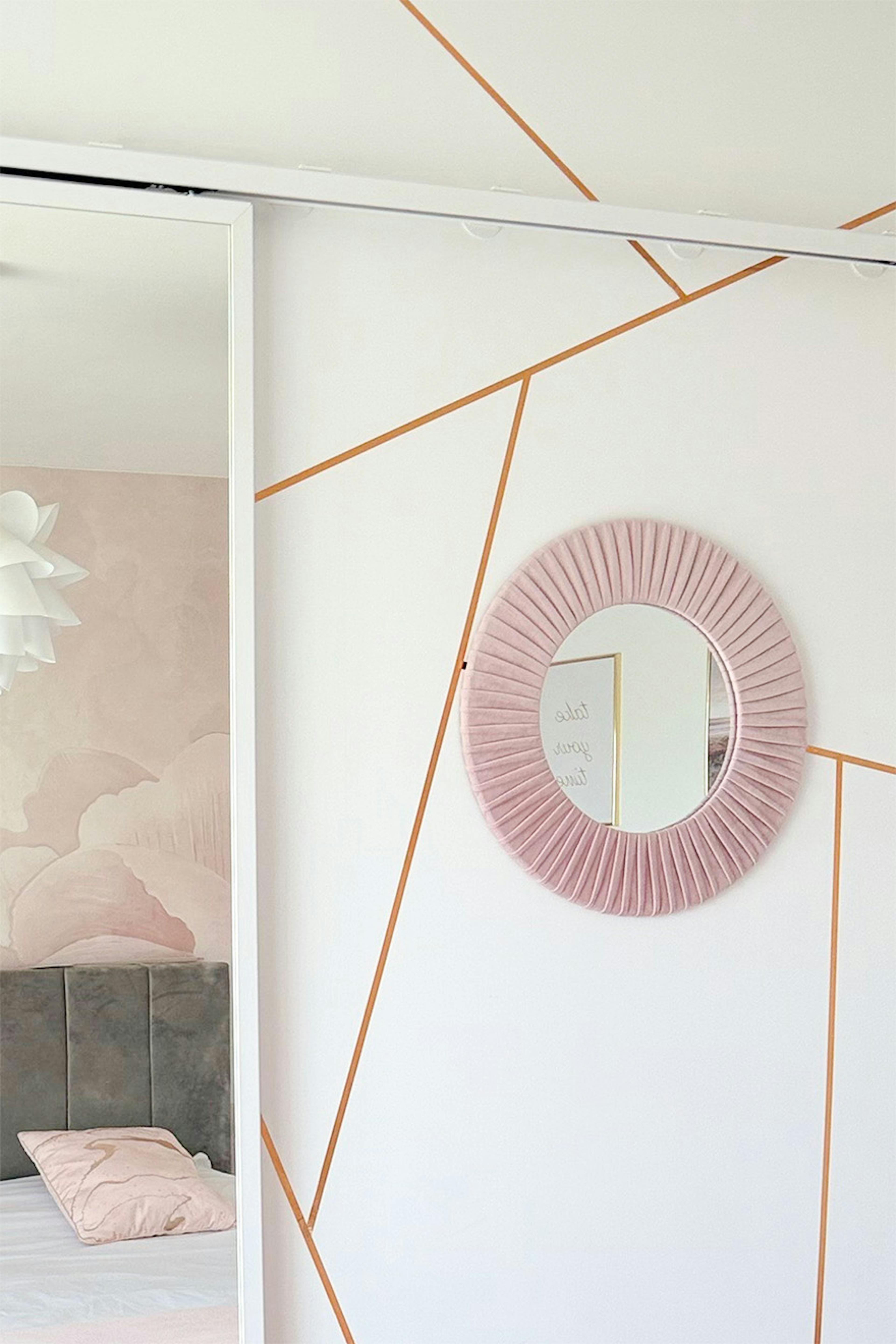 Miroir rond décoratif dans un cadre rose plissé sur un mur géométrique ; chambre à coucher rose poudré et doré.
