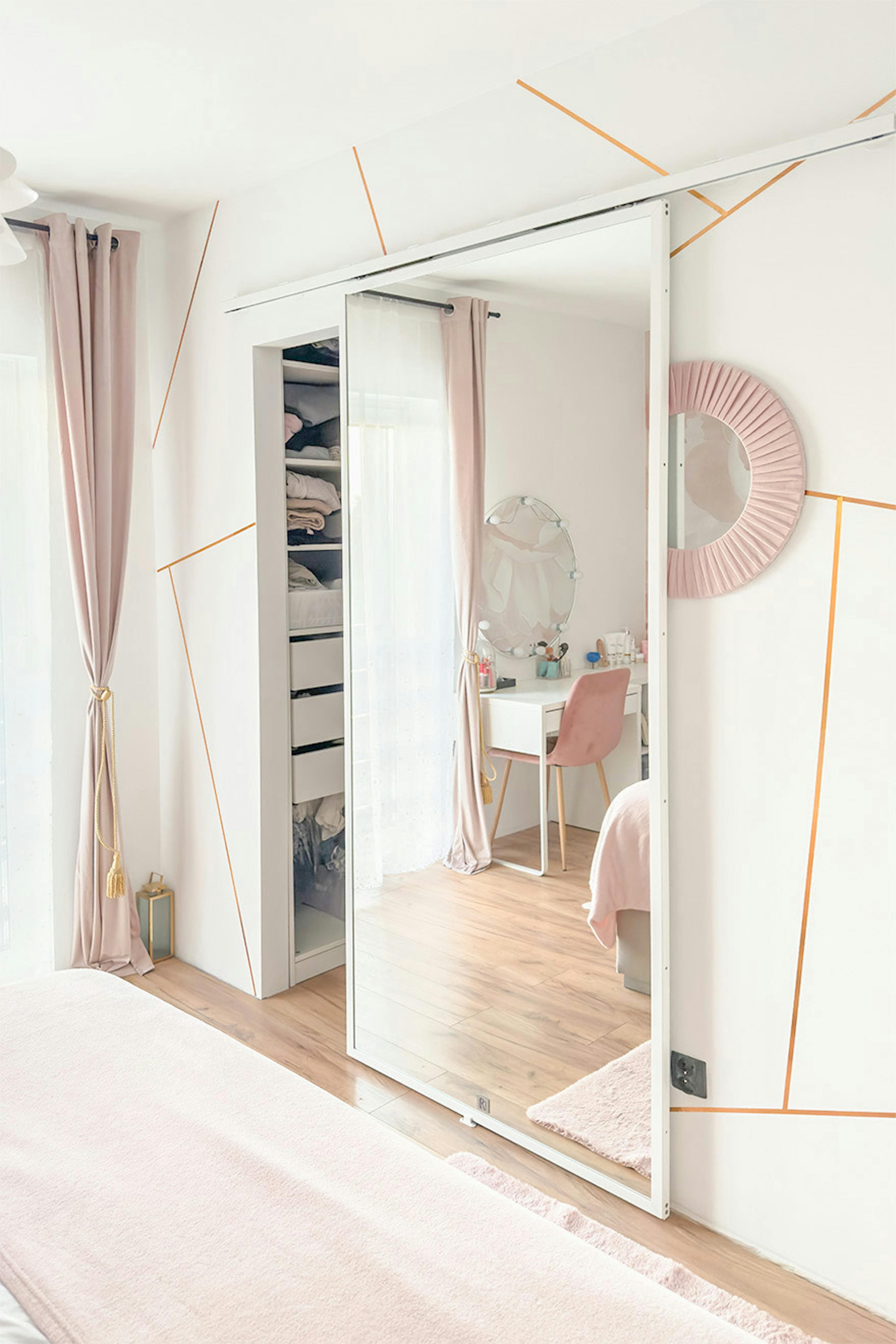 Chambre à coucher avec dressing ouvert ; portes miroir et rideaux en velours rose ; vue sur la coiffeuse blanche.